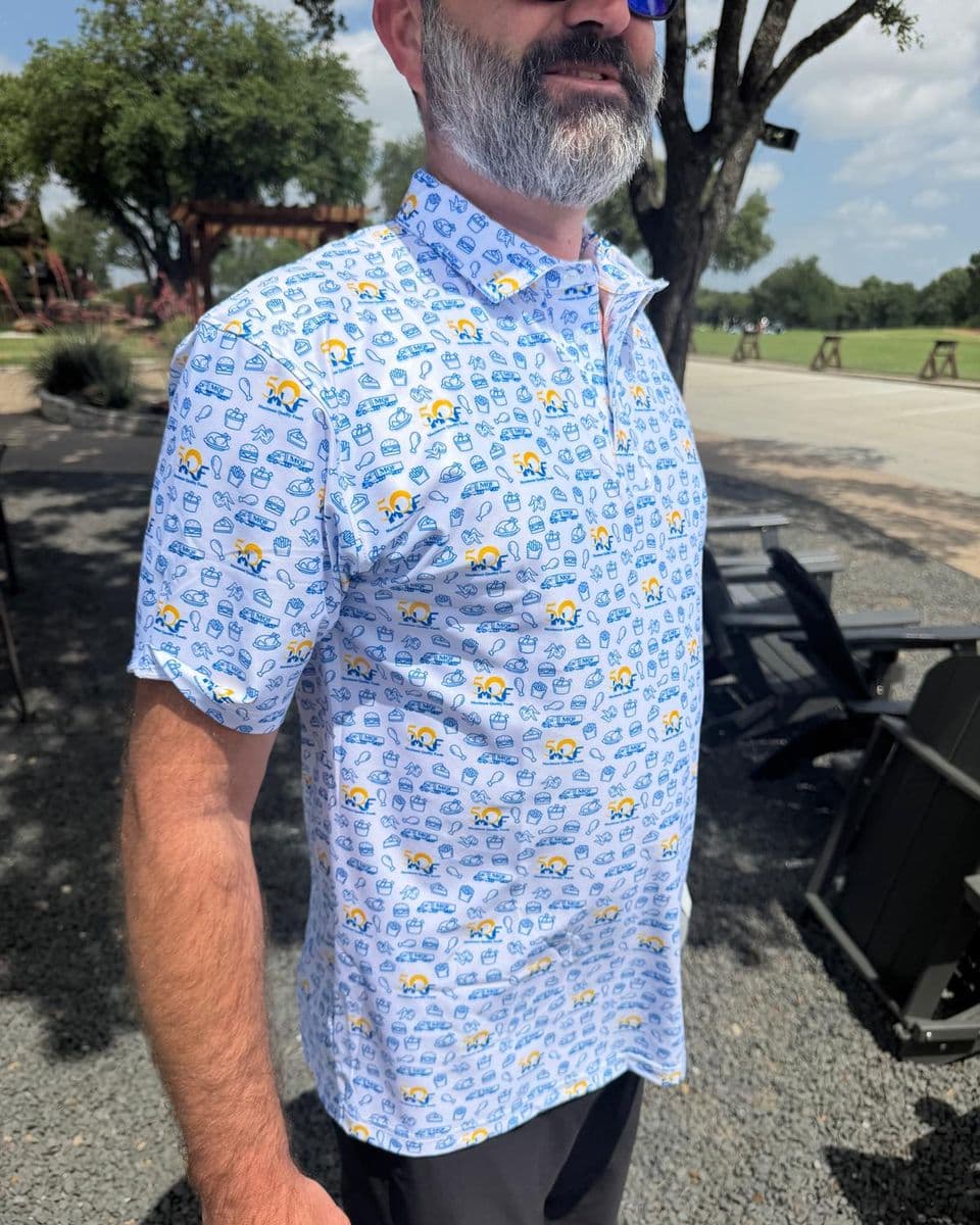 A man outdoors on a sunny patio wearing a white polo with an all-over pattern of small blue icons.