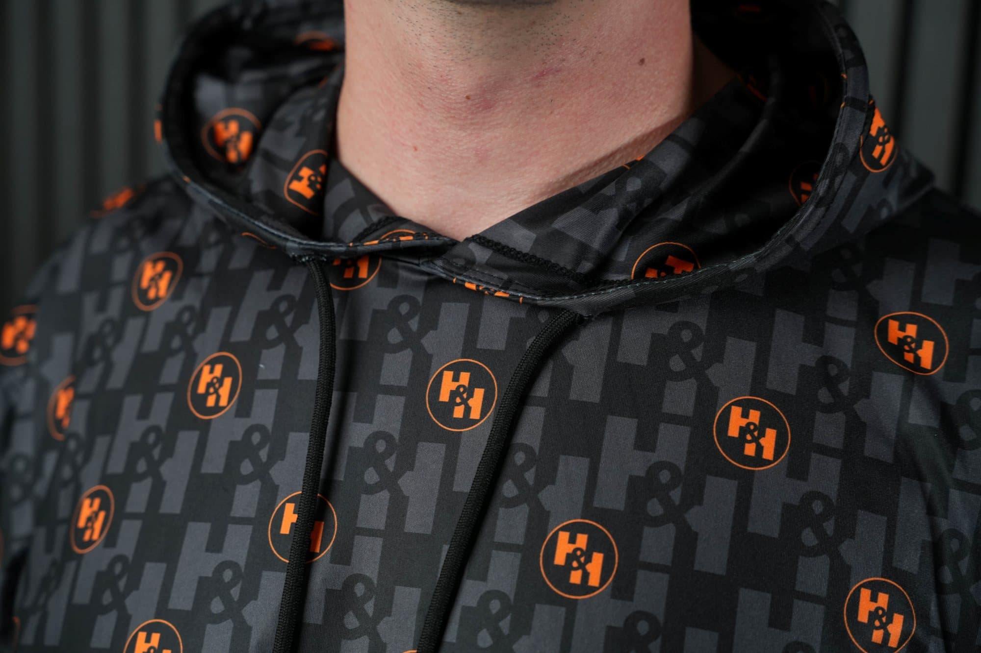 Close-up of a black hooded top with orange circular logos and a tonal pattern