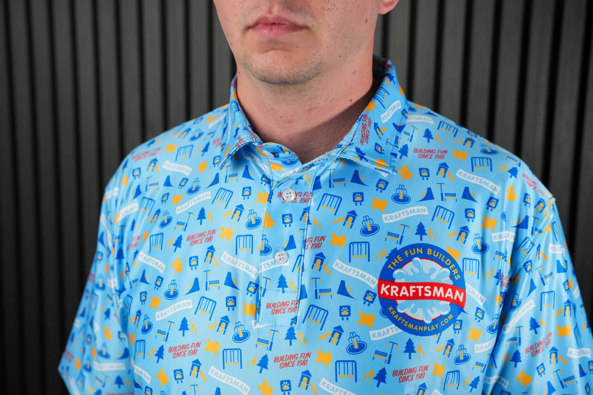 Close-up of a light-blue polo with a yellow, blue and white icon pattern and a round chest badge