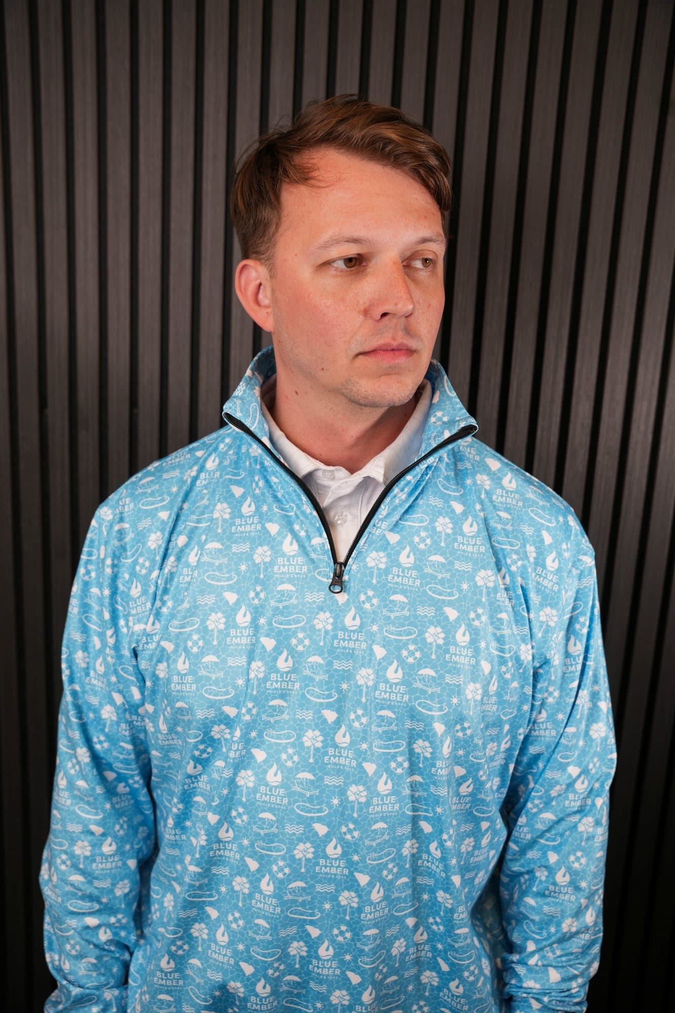 Man in a light-blue all-over print quarter-zip pullover in front of a dark slatted wall