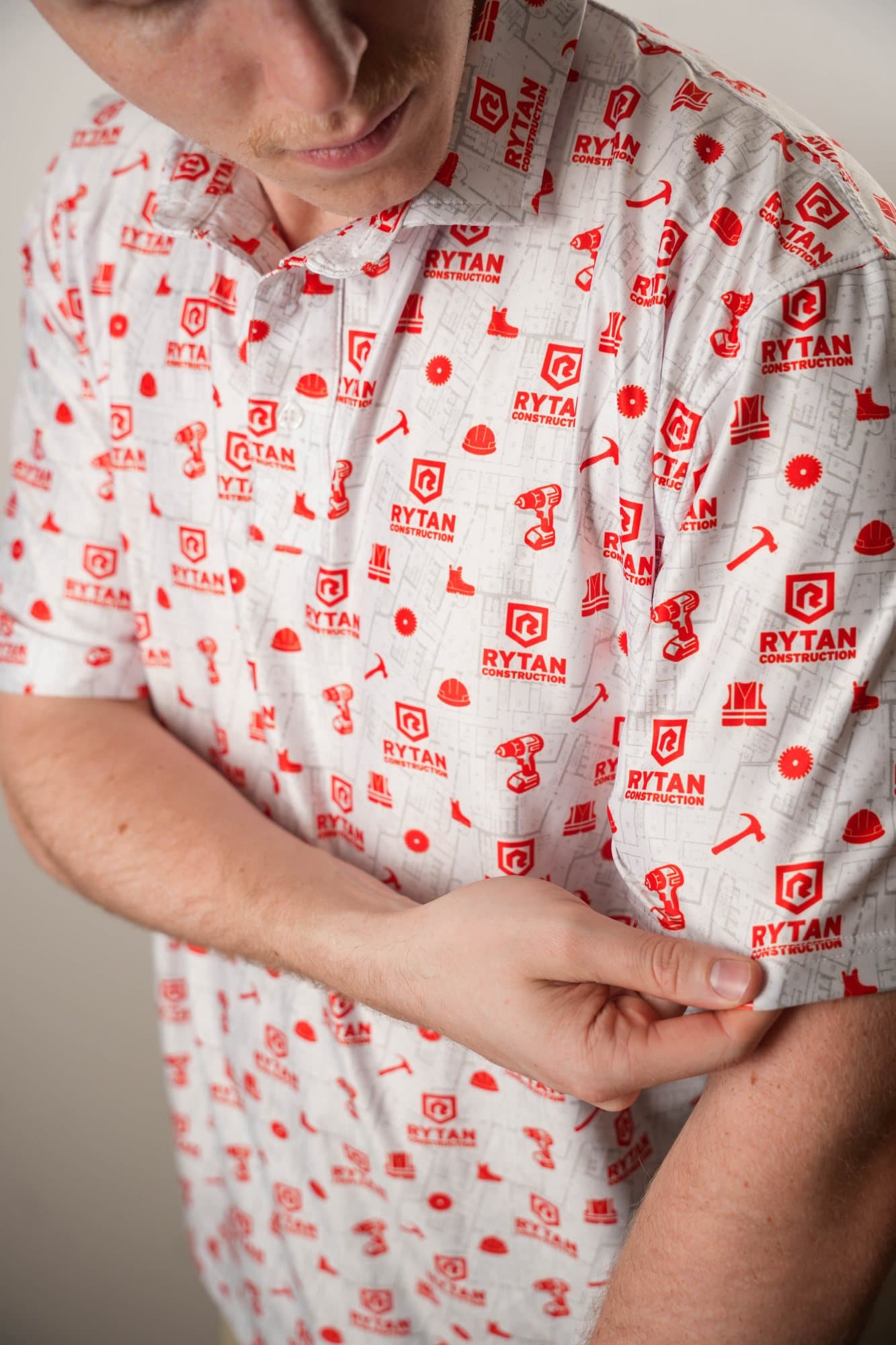 Man in a white polo with red tool and hard-hat icons adjusting his sleeve