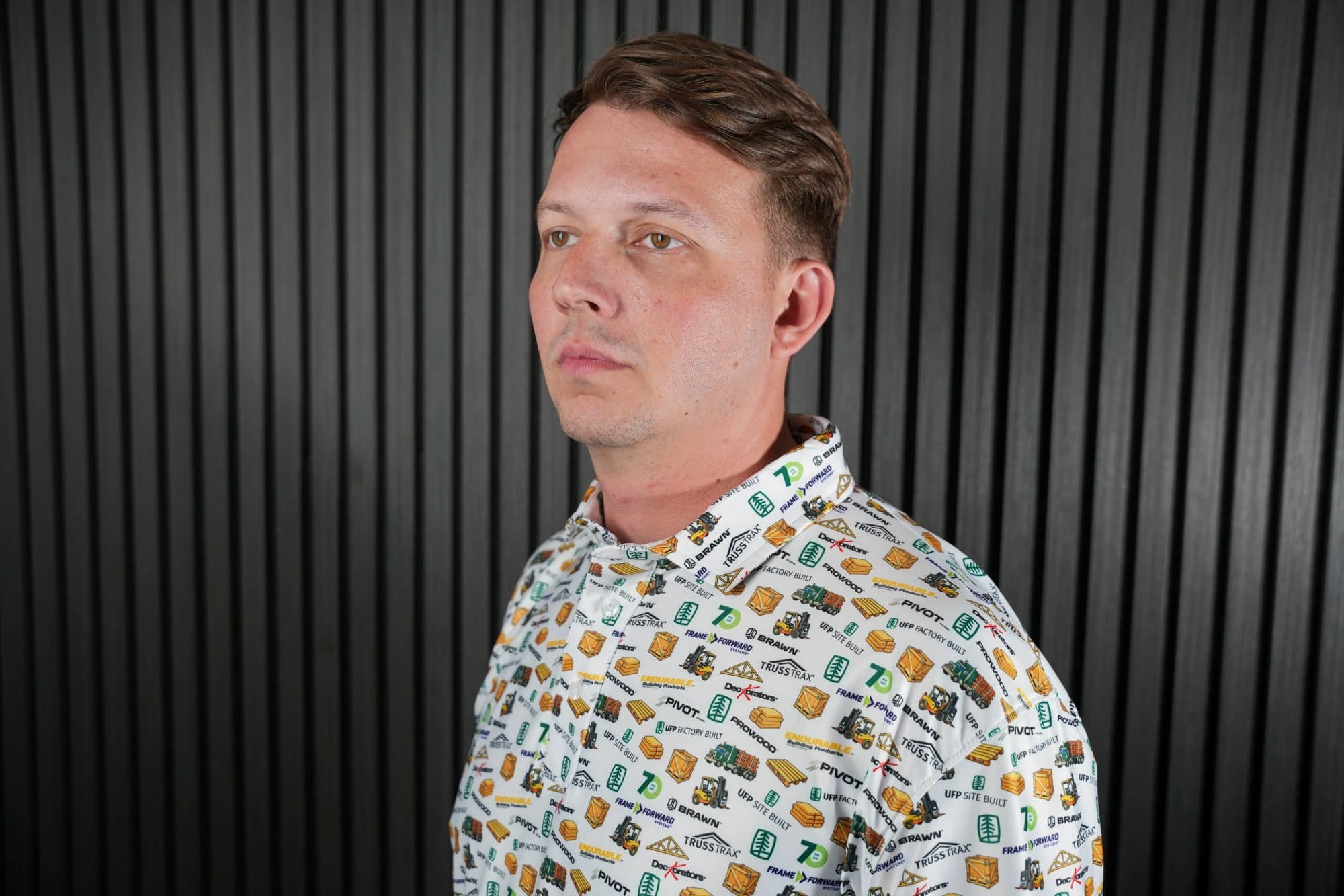Man in a studio wearing a short-sleeve polo printed with a yellow, green and black icon pattern