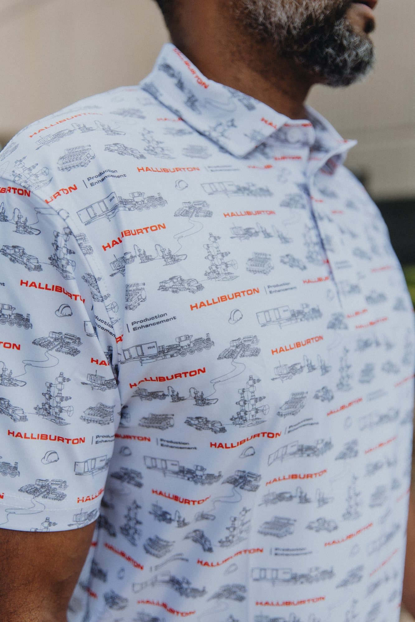 Close-up of a white polo covered in black line-art industrial equipment with orange logos