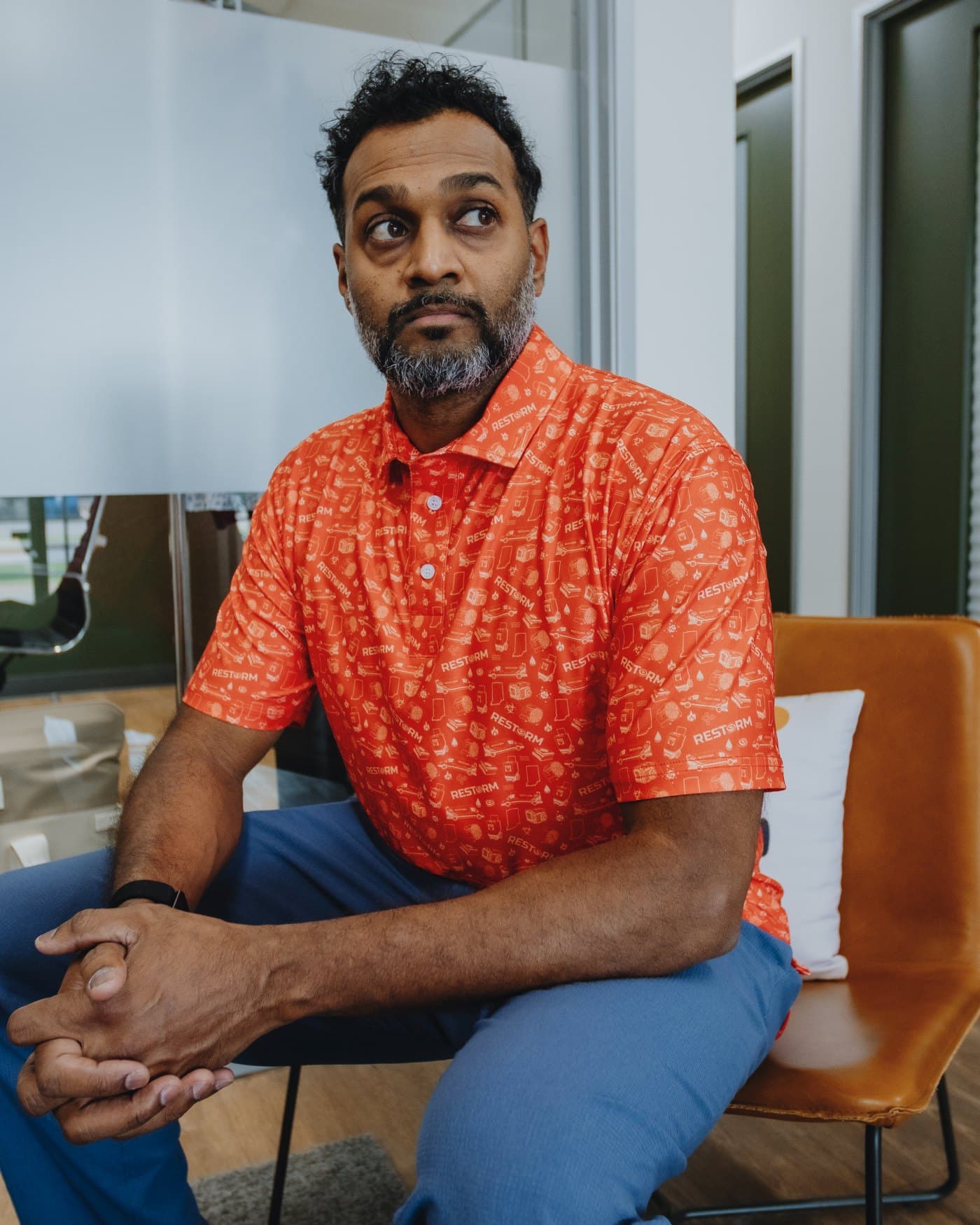 A man seated in an office wearing a bright orange custom all-over print polo