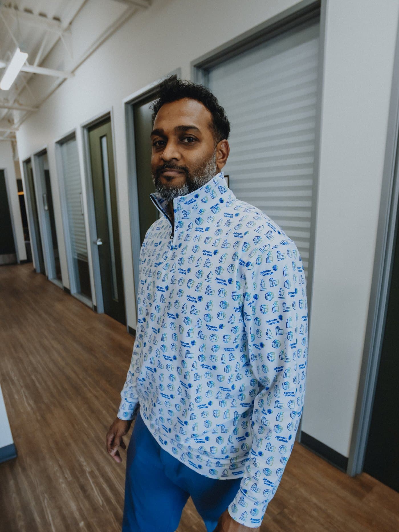 A man in an office hallway wearing a white all-over print quarter-zip pullover