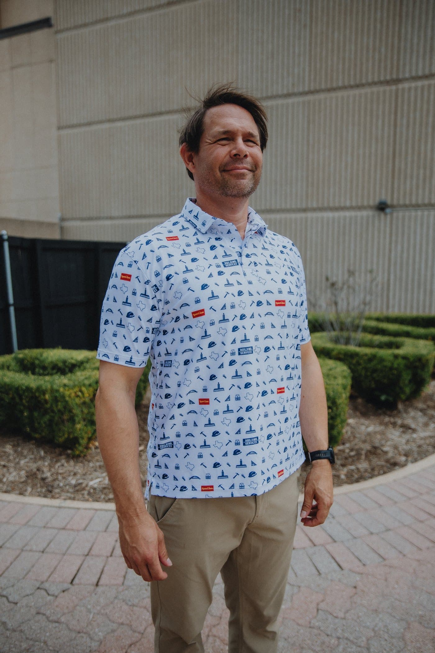 A smiling man outside in a white custom all-over print polo with a construction-themed pattern