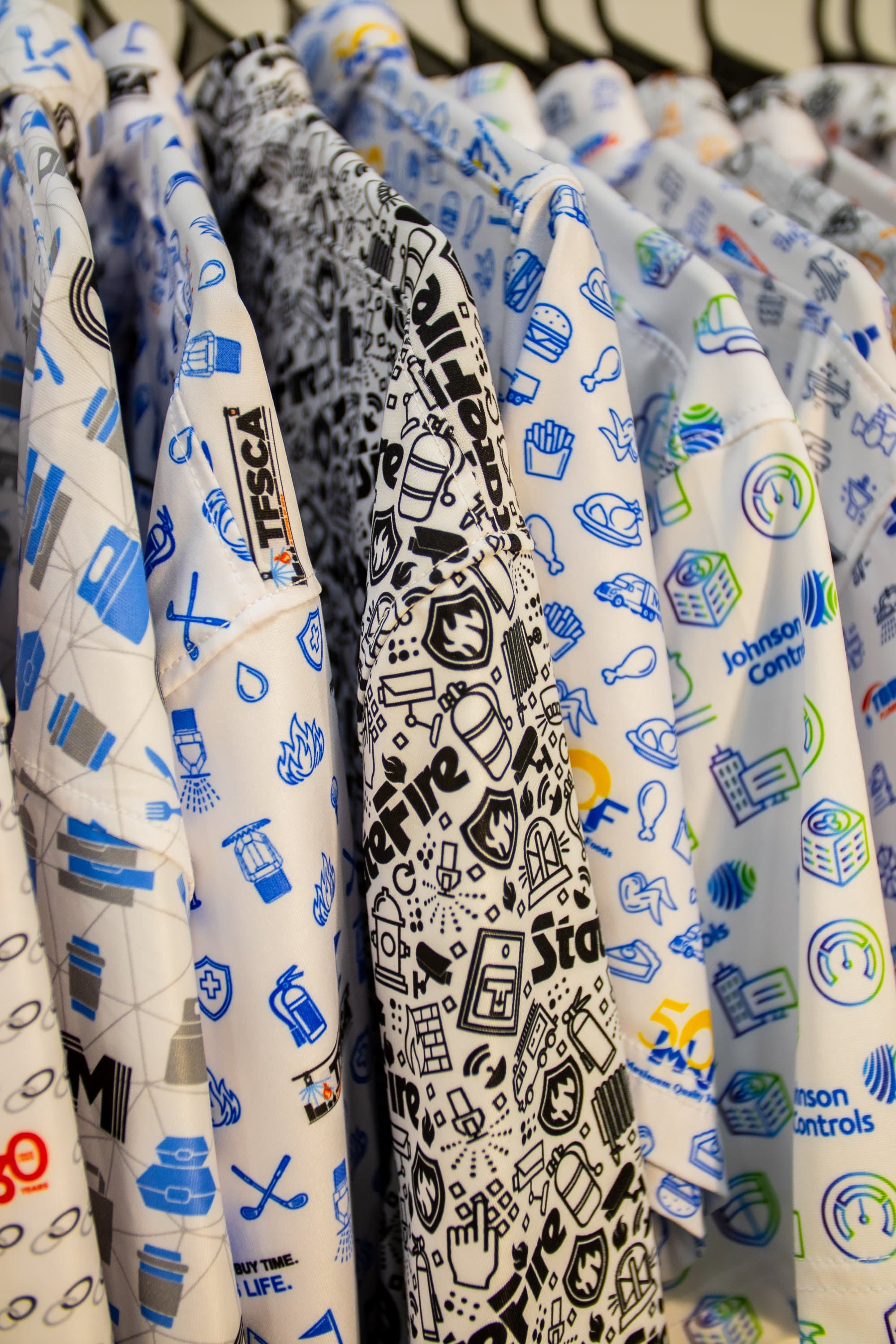 Rack of custom all-over print Uncorp Wear polos with client logos