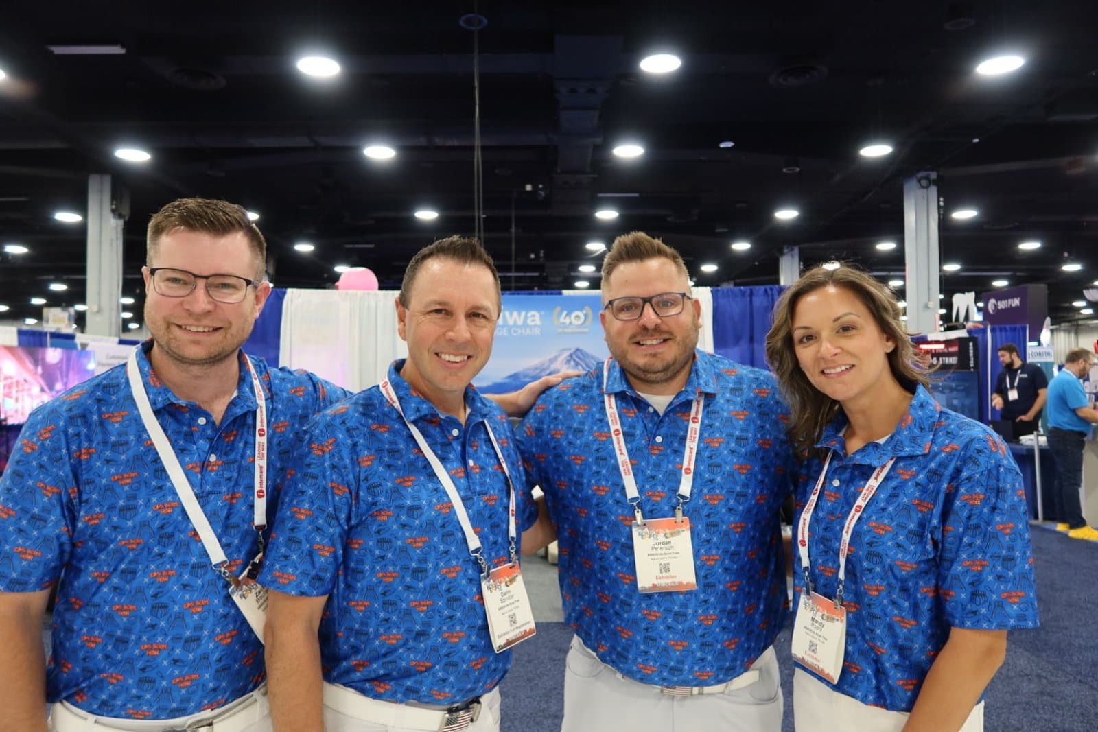 Four smiling coworkers in matching blue custom all-over print polos at a trade show