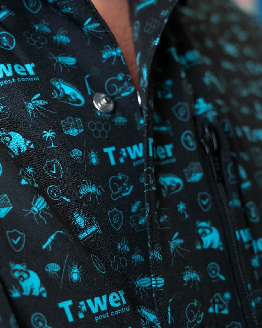Close-up of a black button-up with a teal all-over print, with a metal snap on the placket and a zipper pull to the right of it.
