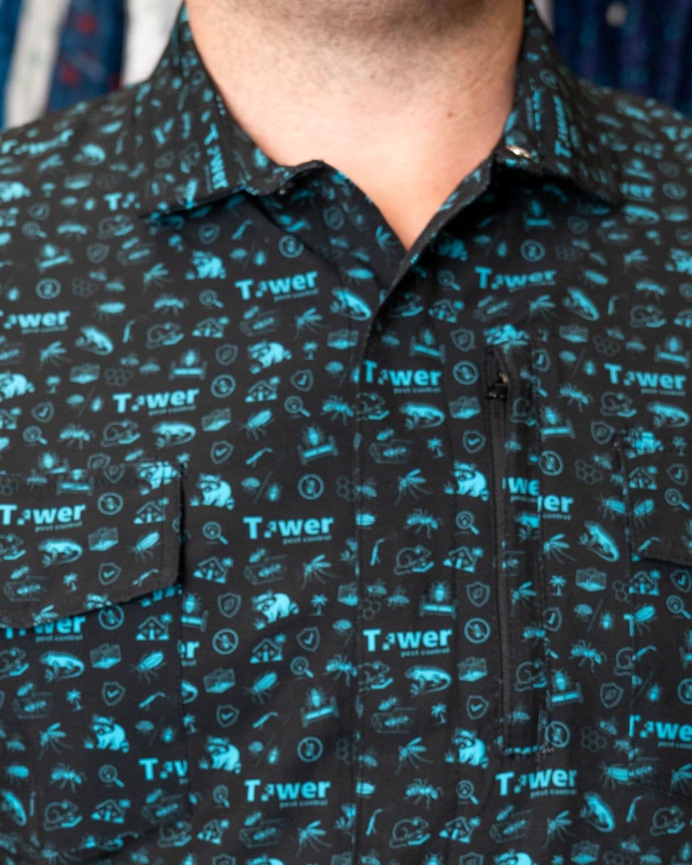 Black button-up with a teal icon-and-wordmark print, with a zip pocket and flap pockets.