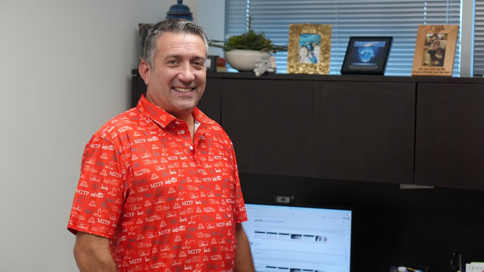 A smiling man in a red custom polo patterned with construction equipment line art